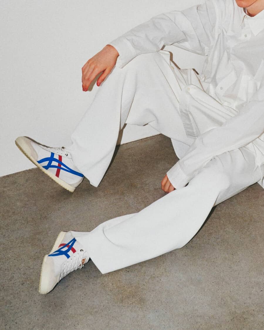 Men's Onitsuka Tiger Mexico 66 sneakers in red, white and blue worn on feet with white pants and a white shirt