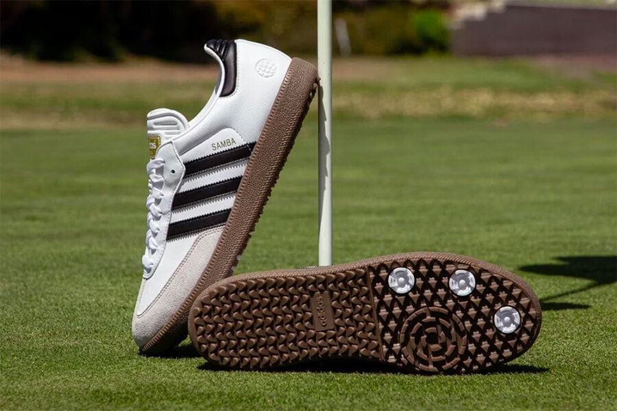 A pair of men's Adidas Samba golf sneakers with spikes on a golf green