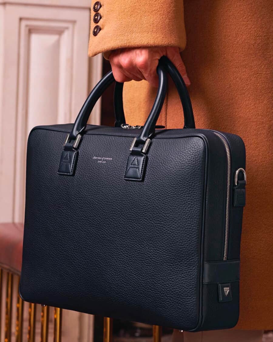 Man in a camel overcoat carrying a luxury Aspinal of London black pebble grain leather briefcase
