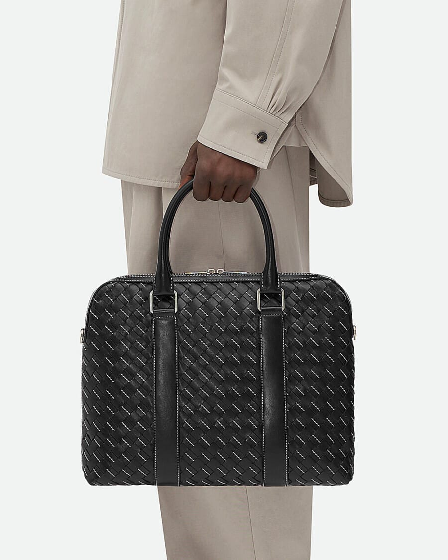 A man holding a black Intrecciato woven leather briefcase by Bottega Veneta