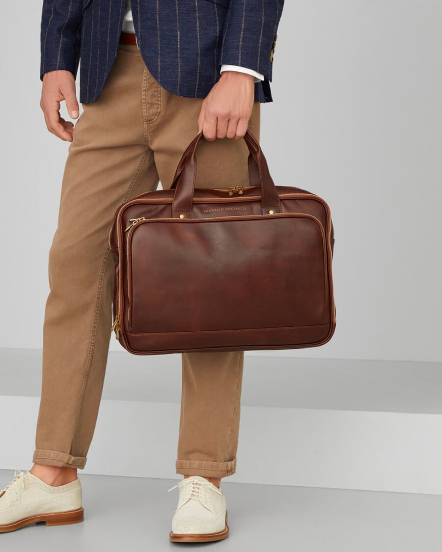 Man in khaki pants and a navy stripe blazer holding a Brunello Cucinelli soft brown leather briefcase