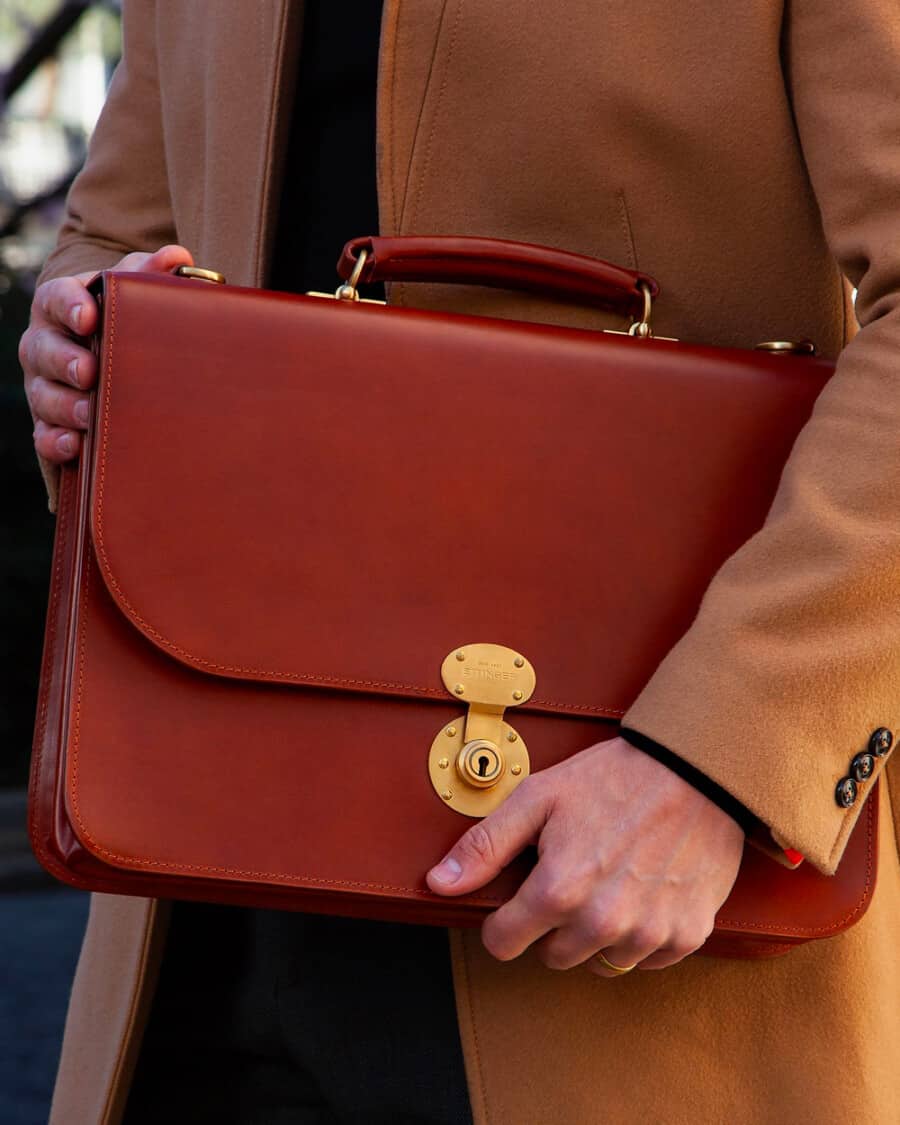 Man in a camel overcoat carrying a luxury brown leather Ettinger briefcase with gold locking mechanism