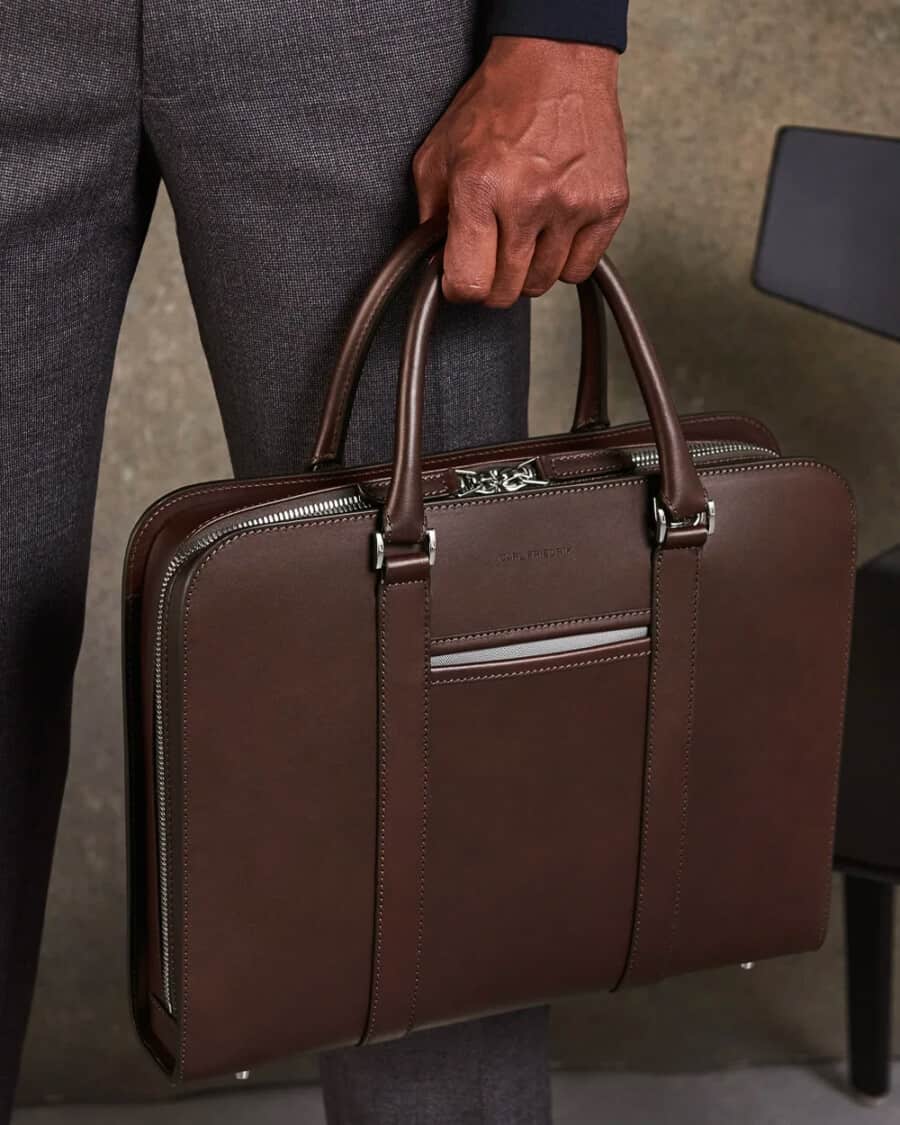 Man in grey wool pants holding a brown leather luxury briefcase by Carl Friedrik