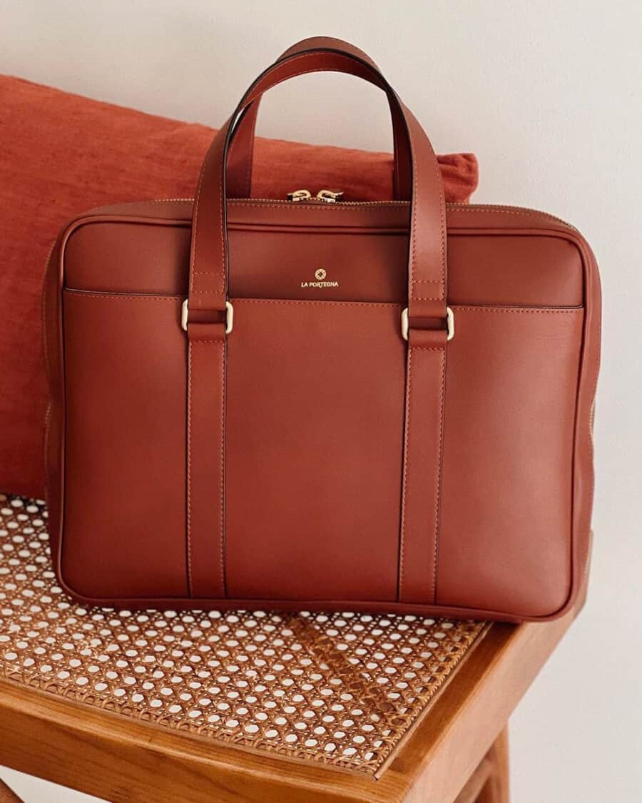 A luxury brown leather La Portegna briefcase on a rattan chair