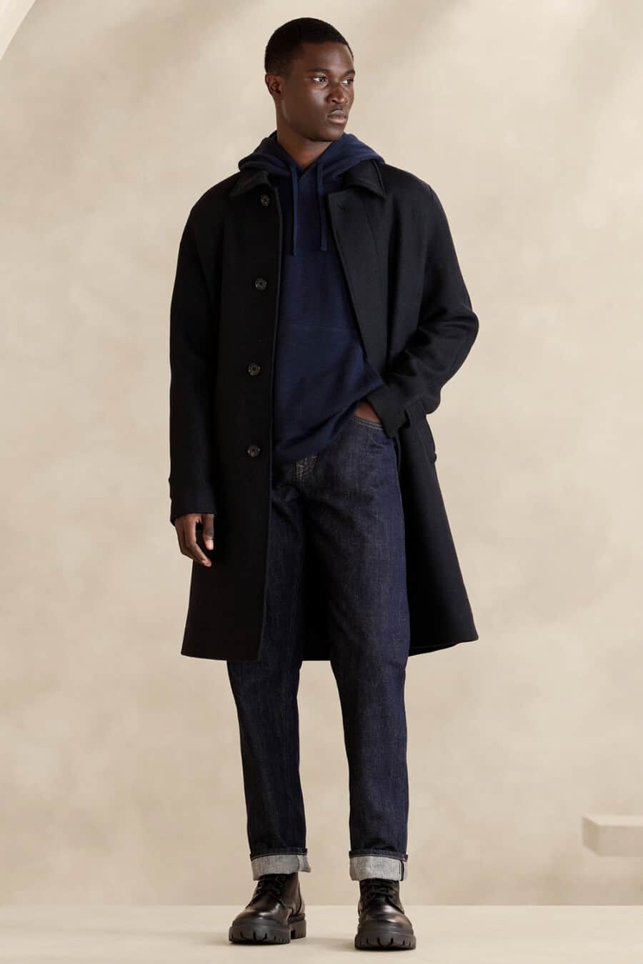 Men's blue raw selvage denim jeans, navy hoodie, navy overcoat and black leather boots outfit