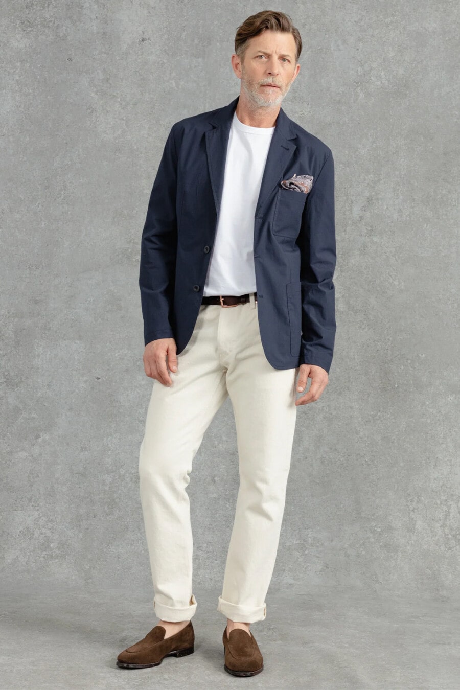 Men's off-white chinos, tucked in white T-shirt, navy unstructured blazer, brown suede Belgian loafers worn sockless and patterned pocket square outfit