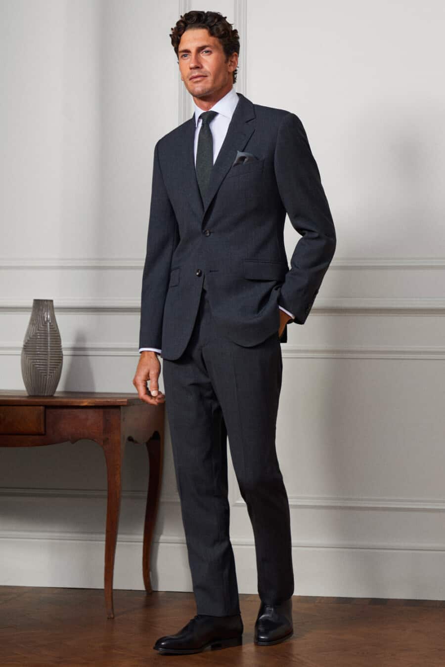 Man wearing a charcoal grey flannel suit by Hackett with a white shirt, grey textured tie and black Oxford shoes
