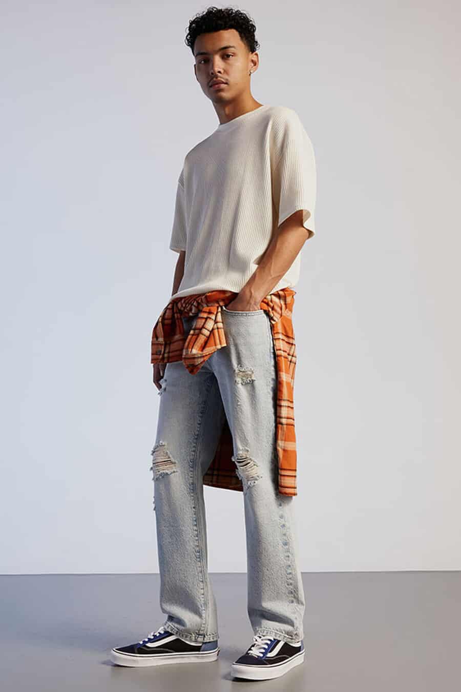 Men's ripped light wash jeans, white oversized T-shirt, orange/yellow check flannel shirt and Vans Authentic sneakers grunge outfit