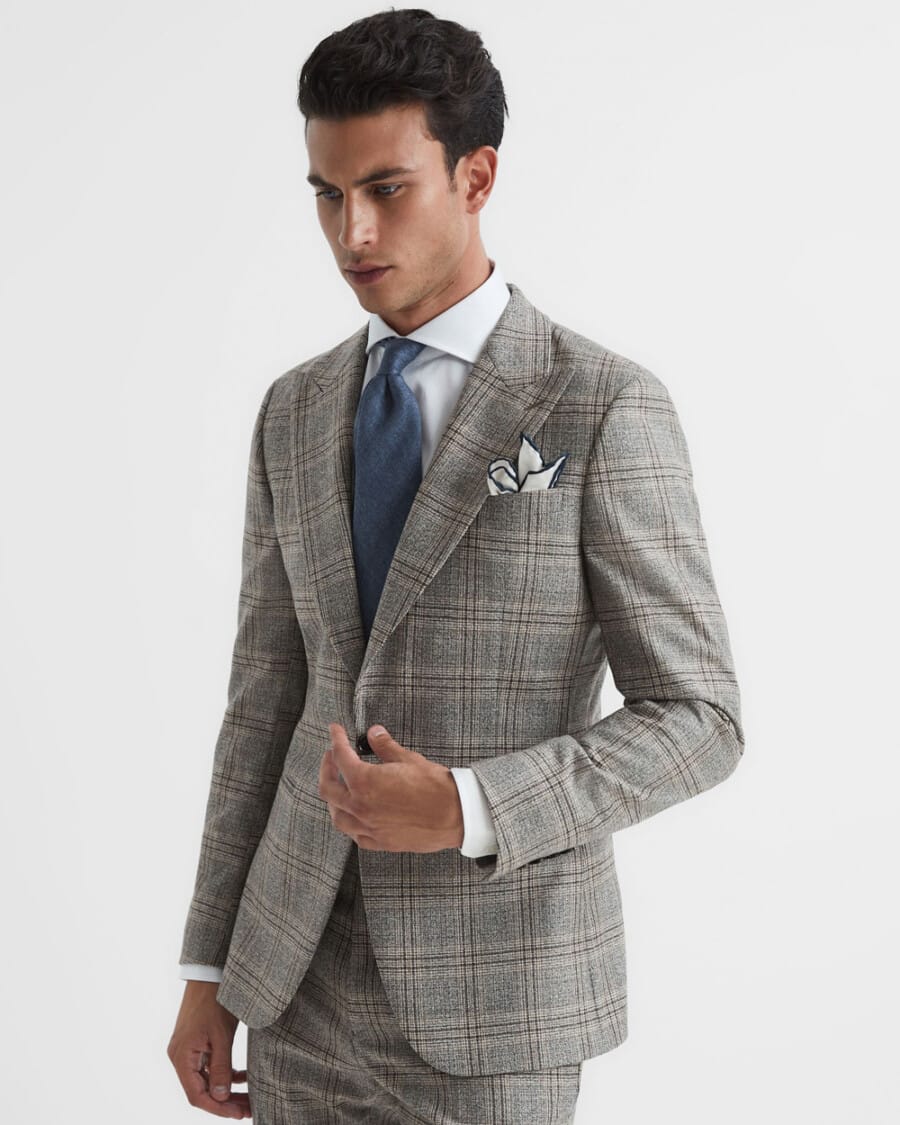 Man wearing a light grey Prince of Wales check suit with a white shirt and blue tie