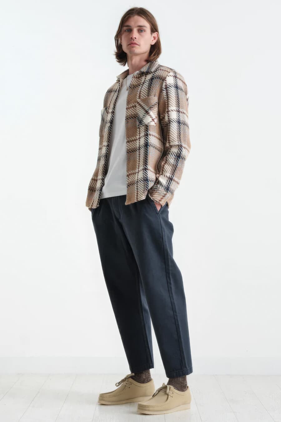 Men's loose, cropped navy pants, white T-shirt, brown check flannel overshirt, brown socks and beige suede Wallabee shoes outfit