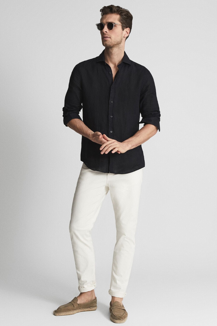 Men's white jeans, black shirt, light brown suede espadrilles and clear frame sunglasses outfit