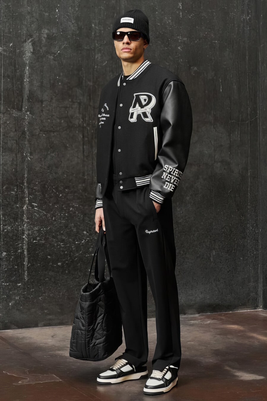 Men's loose black pants, black varsity jacket, black & white chunky sneakers, black sunglasses, black beanie and black tote bag outfit