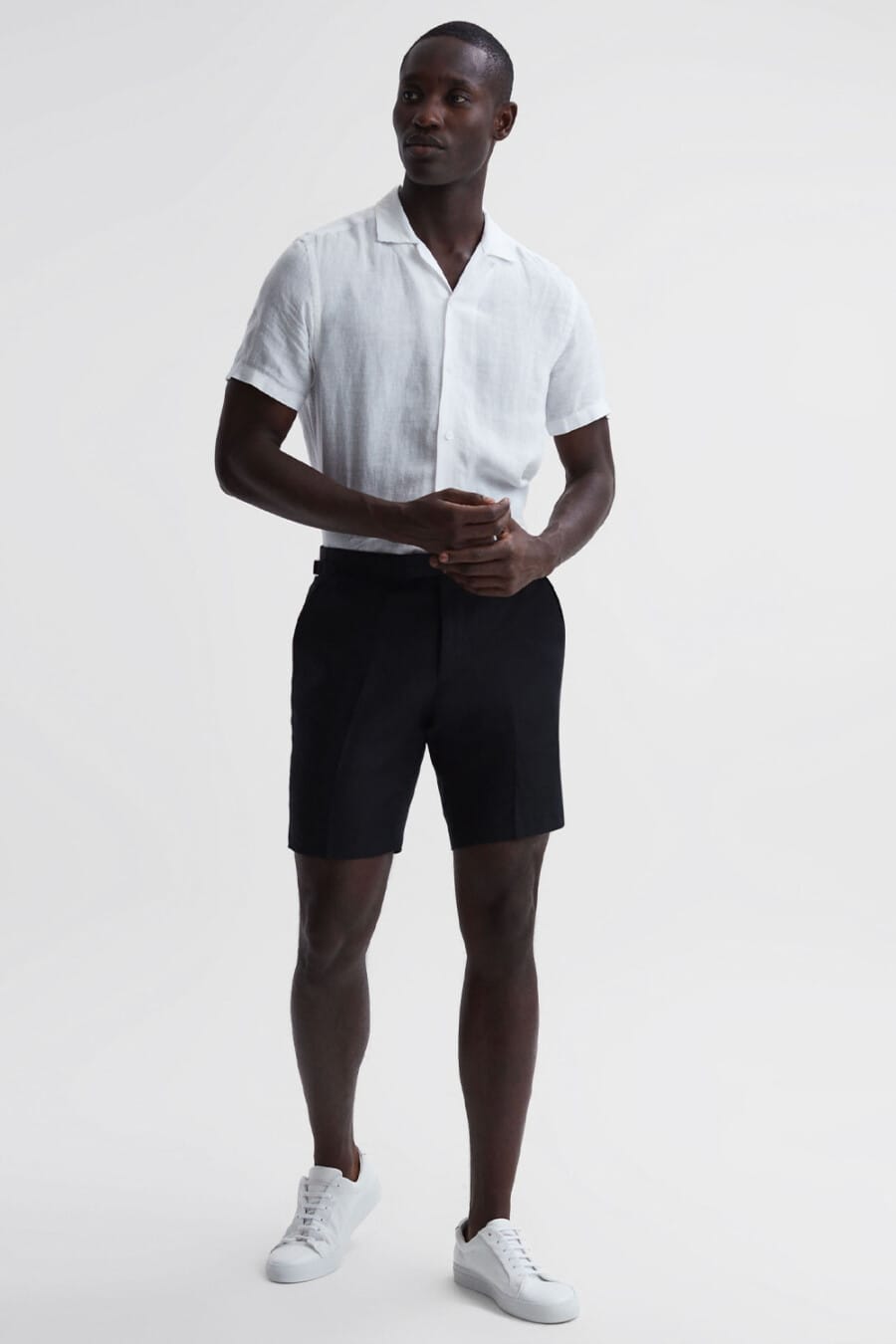 Men's white camp collar shirt tucked into black tailored shorts with white leather sneakers outfit