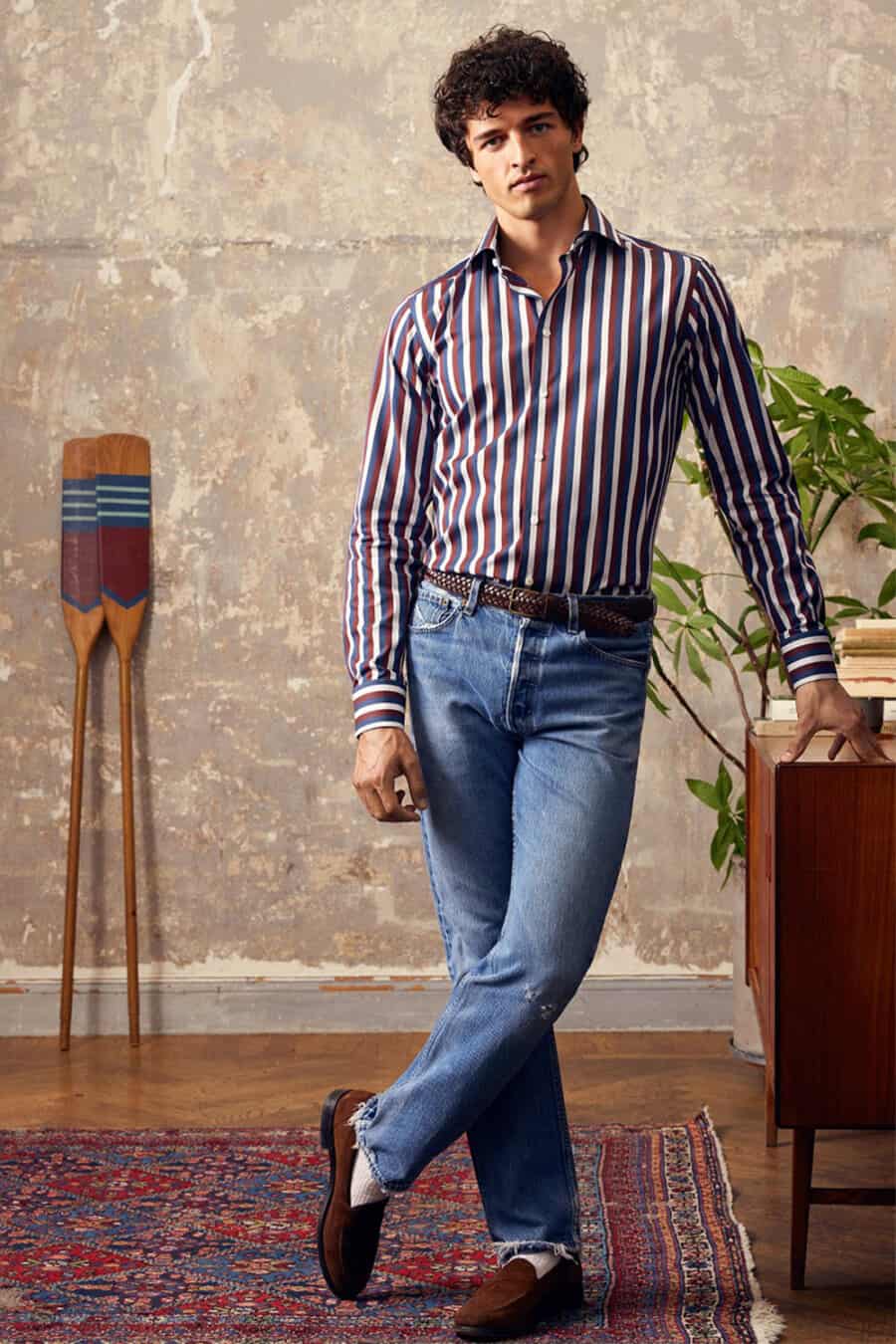 Men's mid-wash jeans, tucked in red/white/blue striped dress shirt, brown woven leather belt, brown suede loafers and white socks outfit