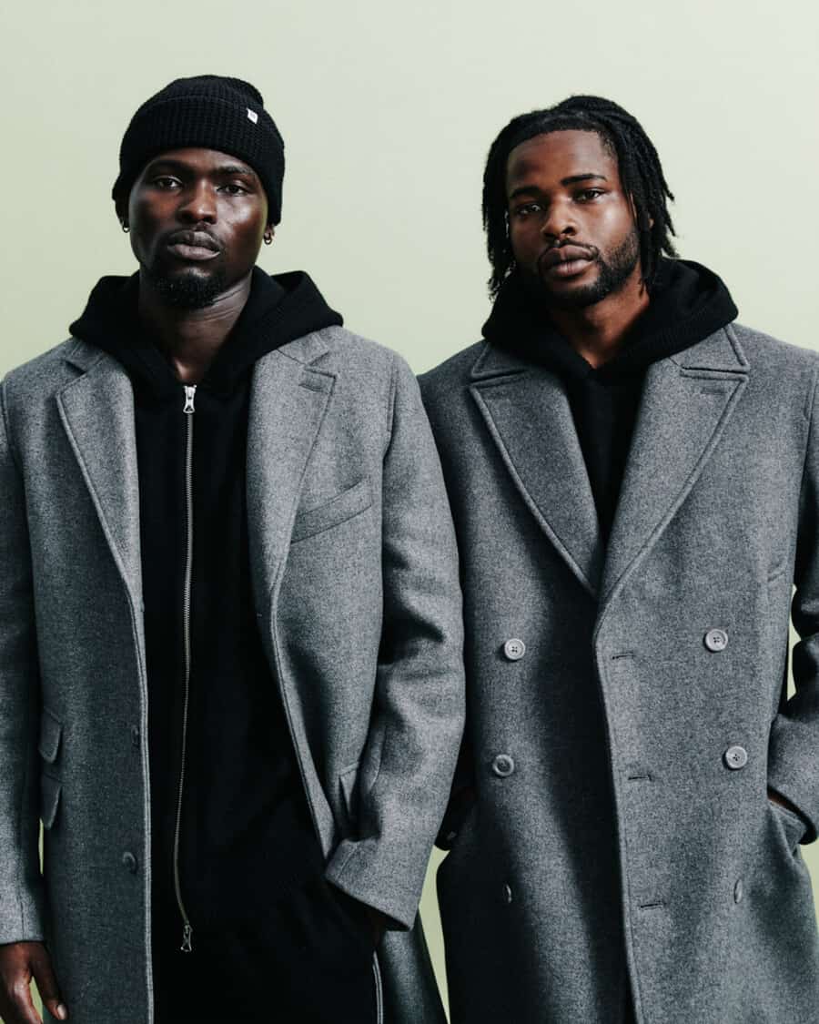 Two men wearing heavyweight black Reigning Champ hoodies underneath grey overcoats