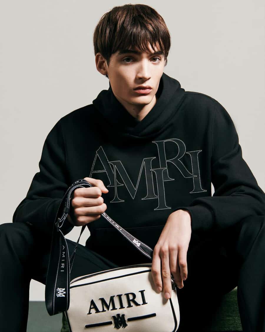 Man wearing black AMIRI logo hoodie and white crossbody bag