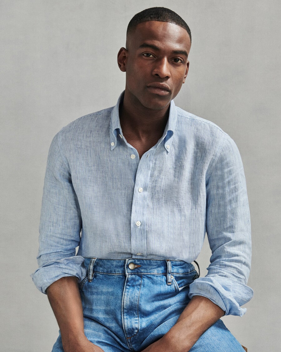 Black man wearing light wash jeans with a tucked in light blue dress shirt