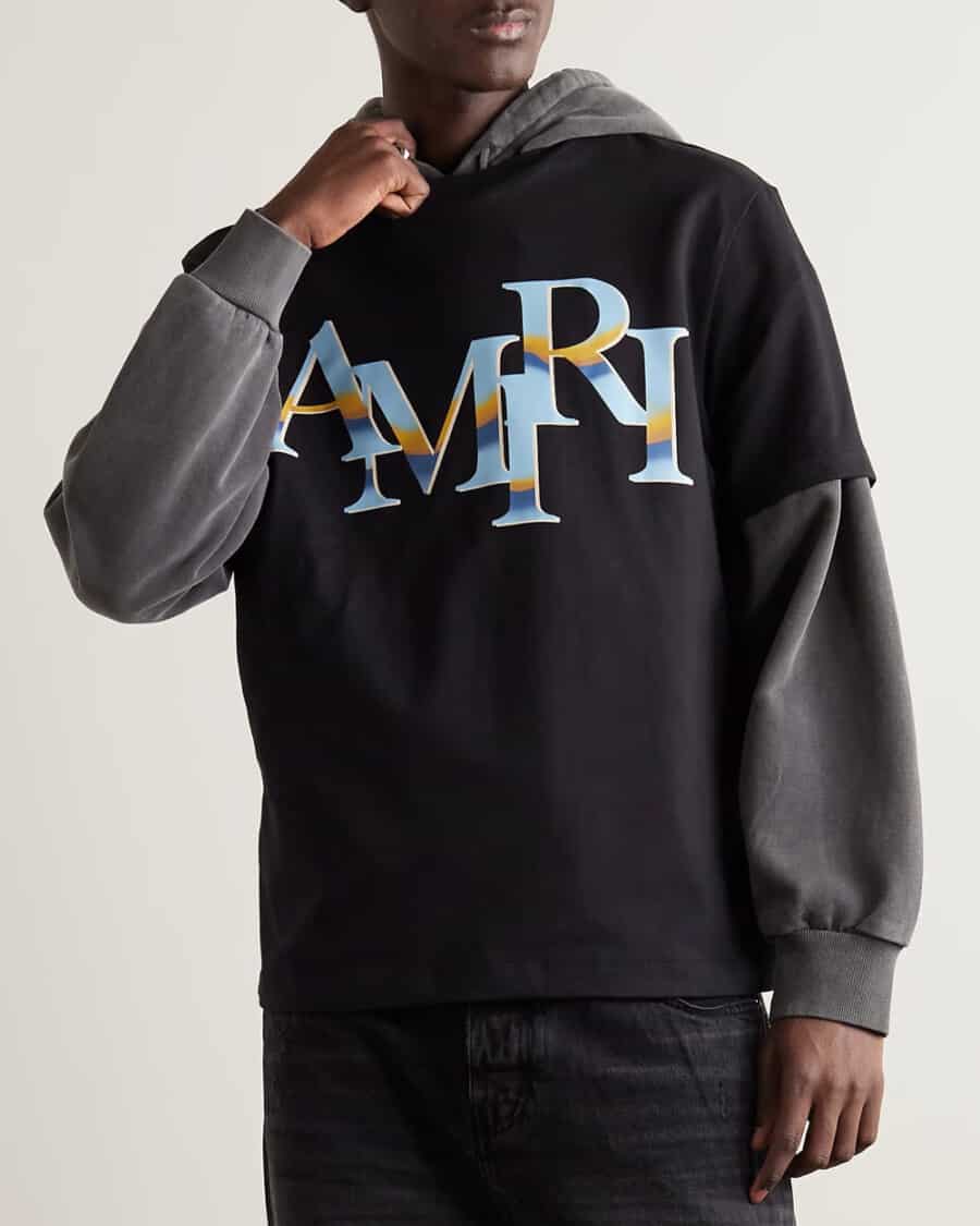 Men's T-shirt trend - man wearing a large AMIRI black logo tee over a grey hoodie with black jeans