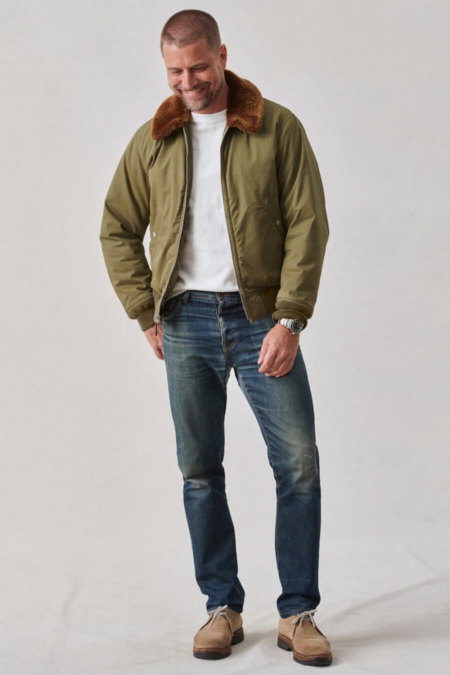 Men's blue jeans, white T-shirt, green brown fur collar bomber jacket and light brown suede shoes outfit