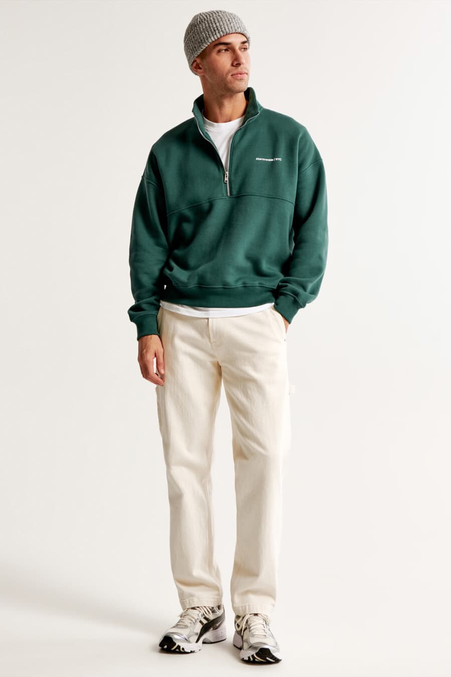 Men's off-white jeans, white T-shirt, green half-zip sweatshirt, grey ribbed beanie and chunky New Balance running shoes outfit