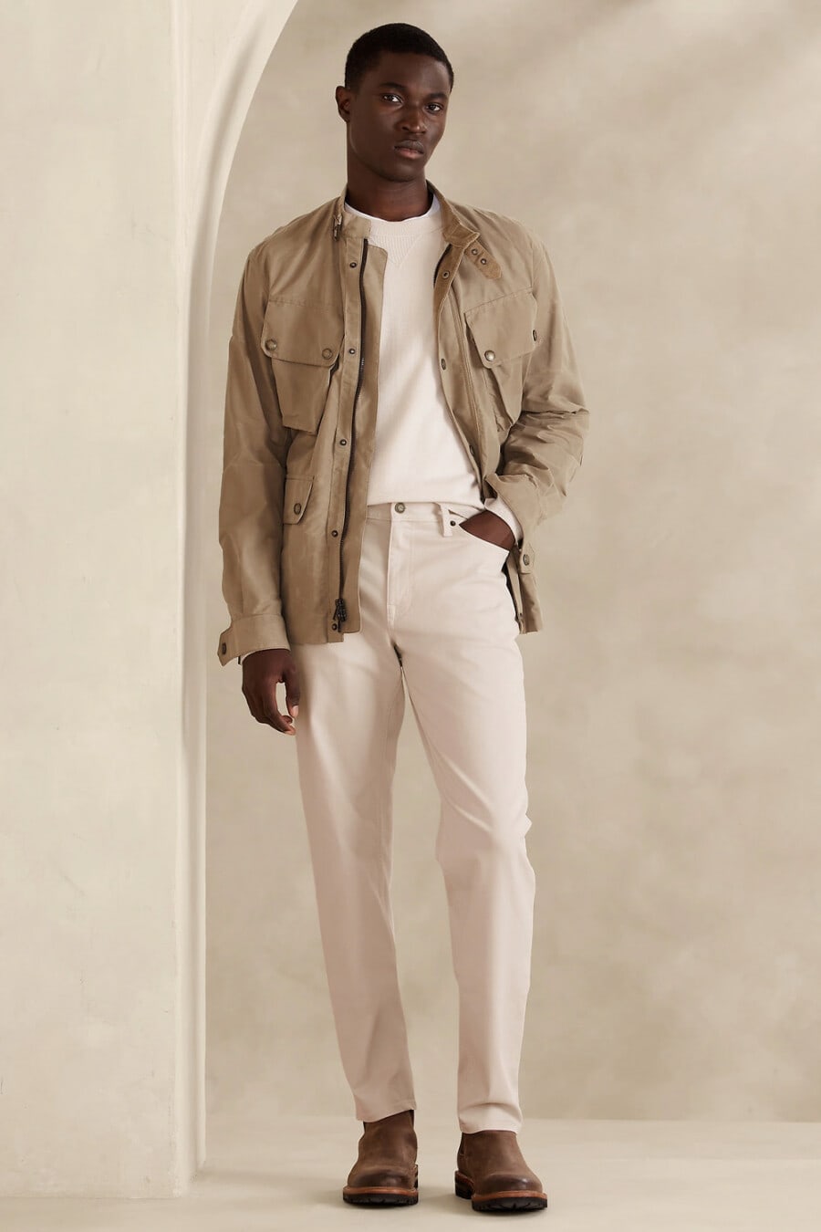 Men's cream pants, white long sleeve top, khaki field jacket and brown leather Chelsea boots outfit